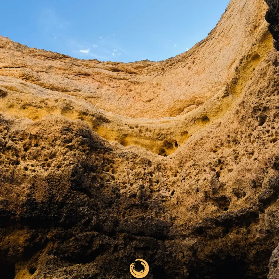 View from inside an Algarve cave, with golden rock walls and blue sky above