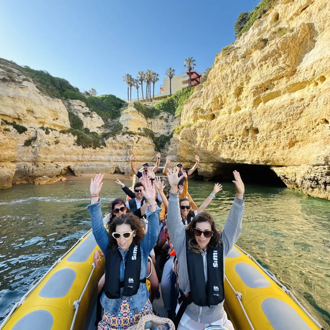 Otter Tours guests raising their arms in excitement aboard the boat with Algarve rock formations in the background