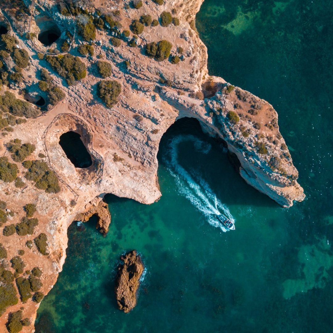 Aerial view of a turquoise shiny sea with a single boat sailing along the coastal cliff in Algarve